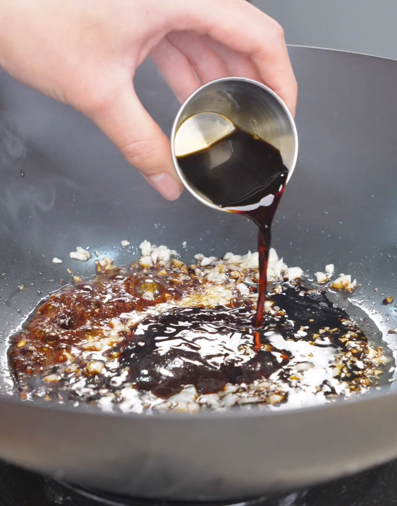 A dark hoisin and soy sauce being poured over the fragrant garlic in the pan for Hoisin Garlic Noodles Recipe.