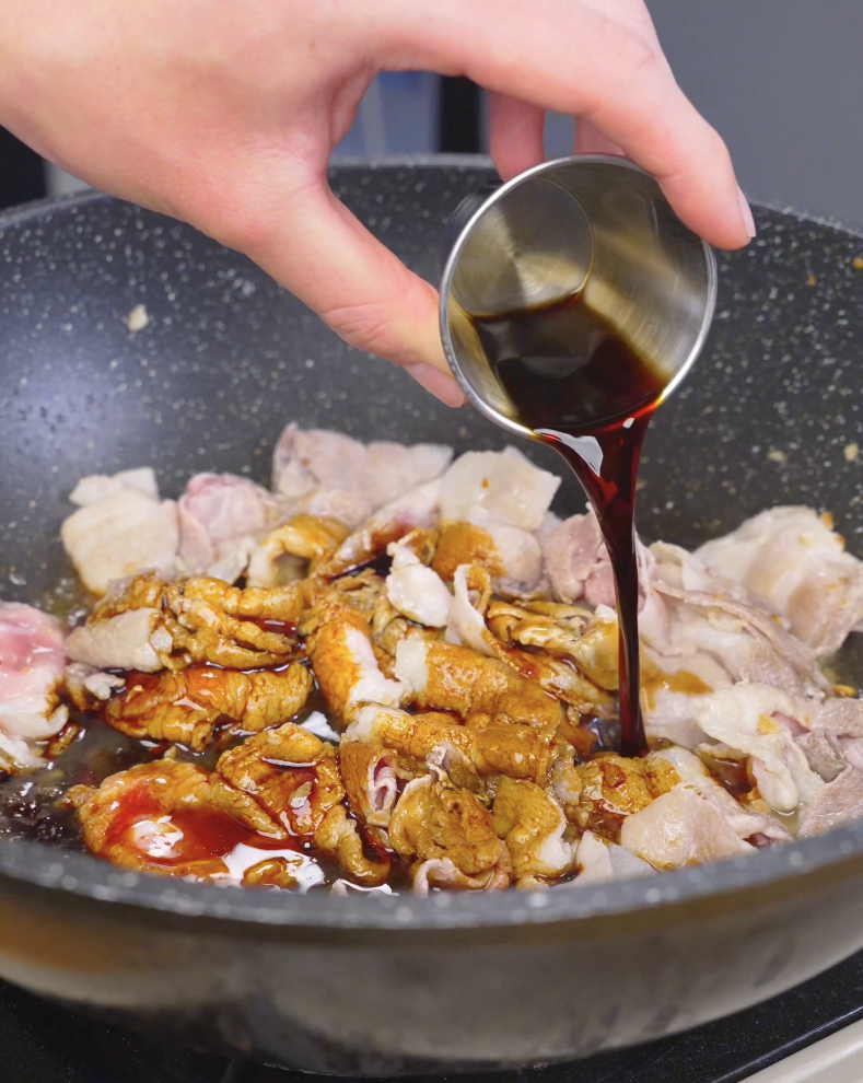 Dark soy sauce being poured over the browning pork in the pan for Sticky Sweet Pork Belly Recipe.