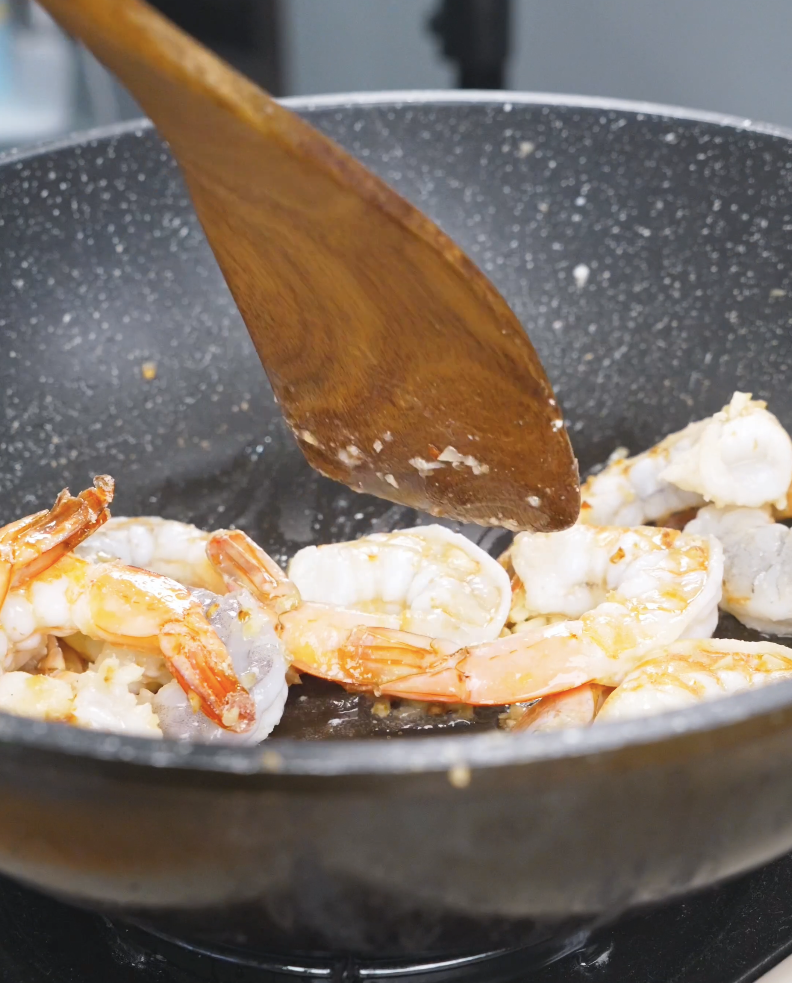 Raw peeled shrimp being added to the garlic in the pan for Honey Garlic Shrimp Recipe.