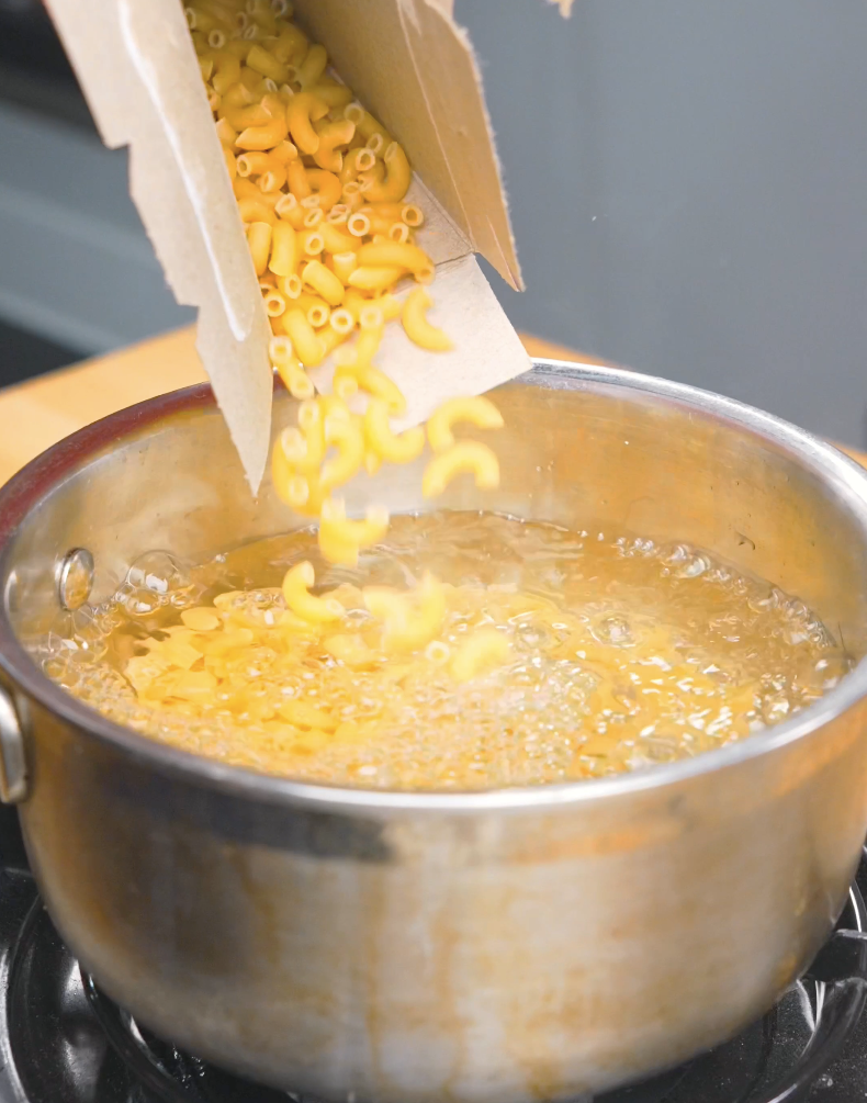 Elbow macaroni being poured into a pot of boiling water for Hawaiian Mac Salad Recipe.