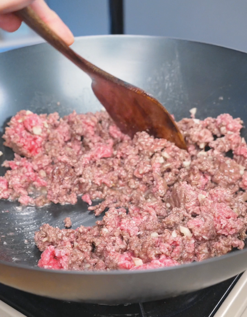 Ground beef being broken up and browned with a wooden spatula while making Garlic Ground Beef Recipe.
