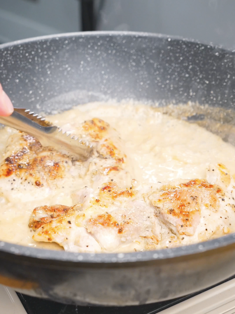 Seared chicken thighs being returned to the pan and coated in cream sauce for Creamy Garlic Chicken Pasta Recipe.