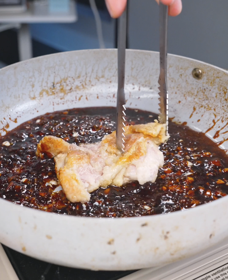 Fried chicken being turned with tongs to coat it in the glossy sauce for Crispy Sticky Sweet Chicken Recipe.