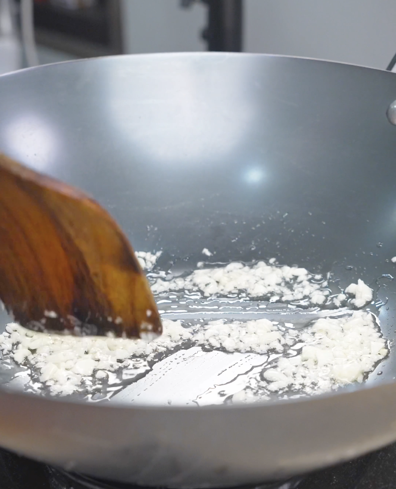Minced garlic being cooked in oil in a wok while starting Hoisin Garlic Noodles Recipe.