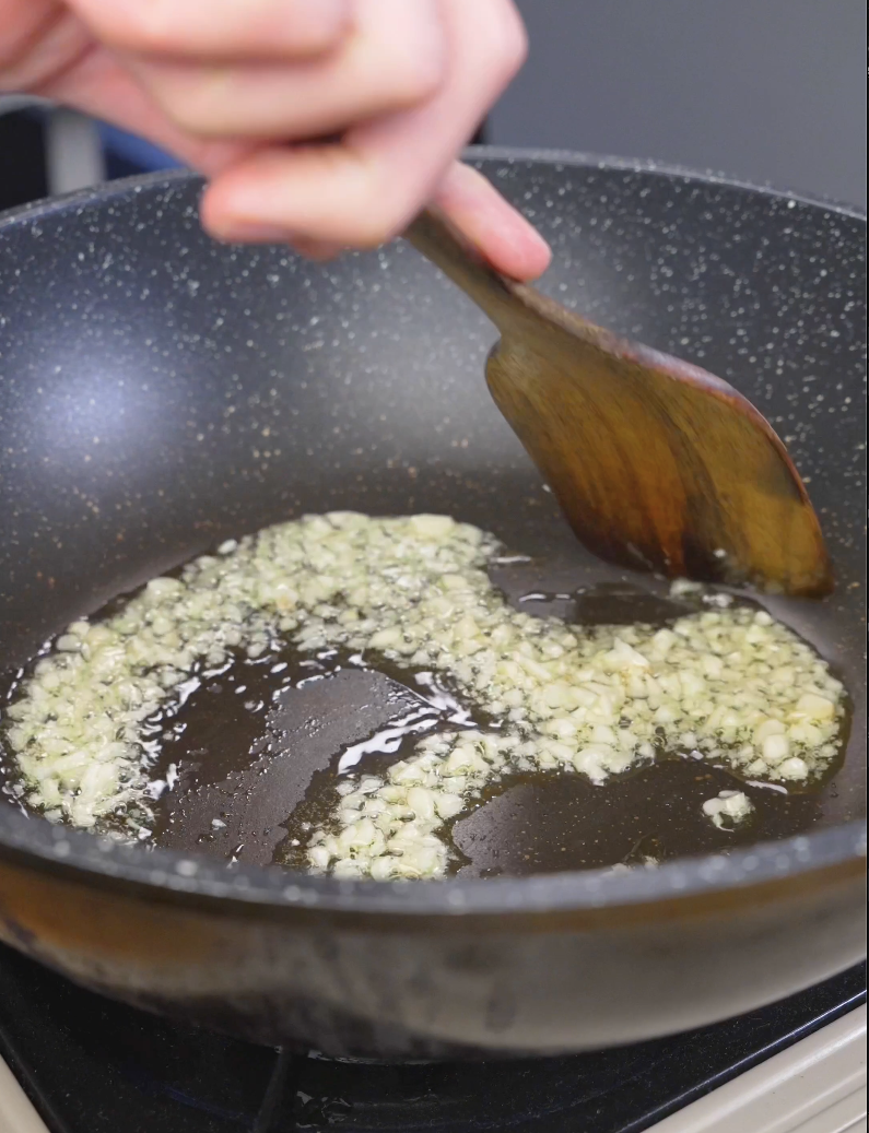 Minced garlic sizzling in oil in a pan while starting Sticky Sweet Pork Belly Recipe.