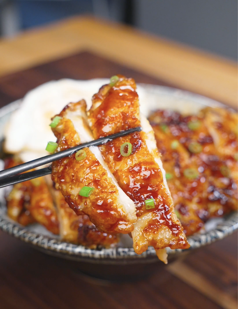Chopsticks holding a saucy slice above the bowl of Crispy Sticky Sweet Chicken Recipe.
