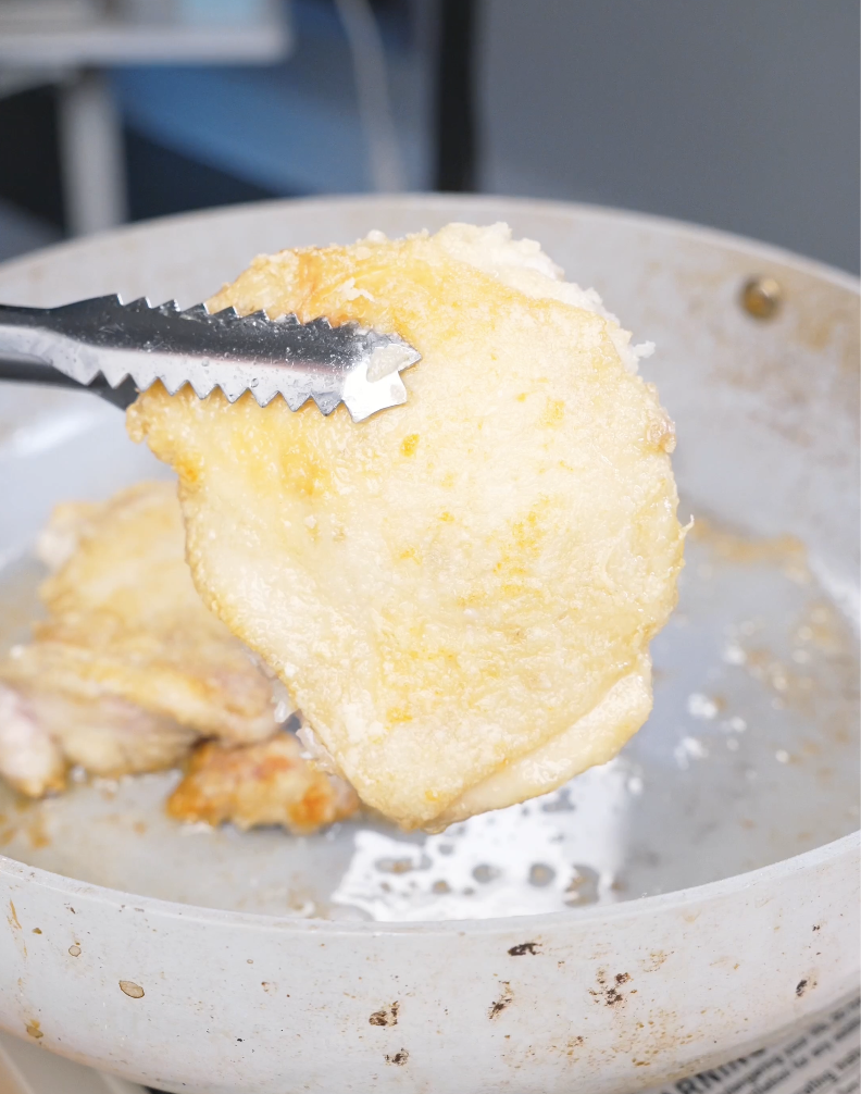 Tongs lifting a golden, crispy fried chicken piece from hot oil while making Crispy Sticky Sweet Chicken Recipe.