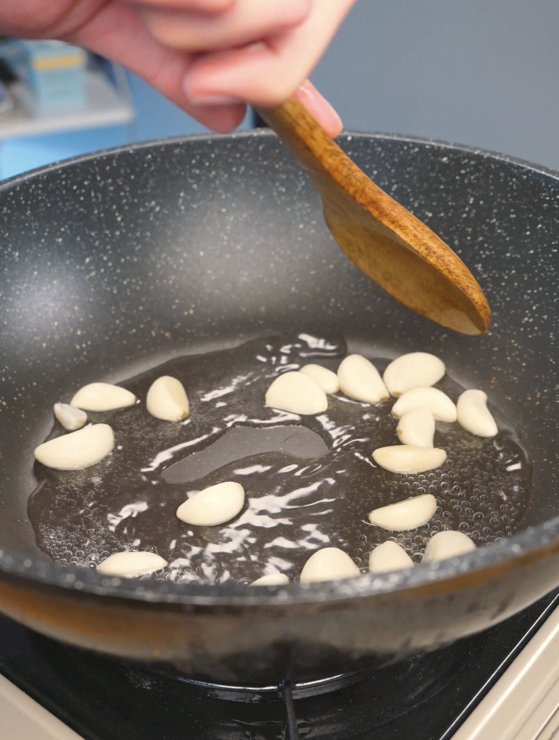 Whole garlic cloves frying in oil in a pan while starting Sticky Garlic Chicken Recipe.