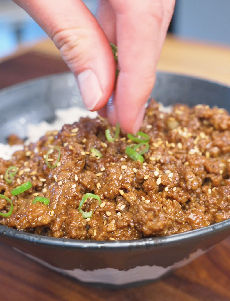 Sliced green onions being sprinkled by hand over a bowl of Garlic Ground Beef Recipe.