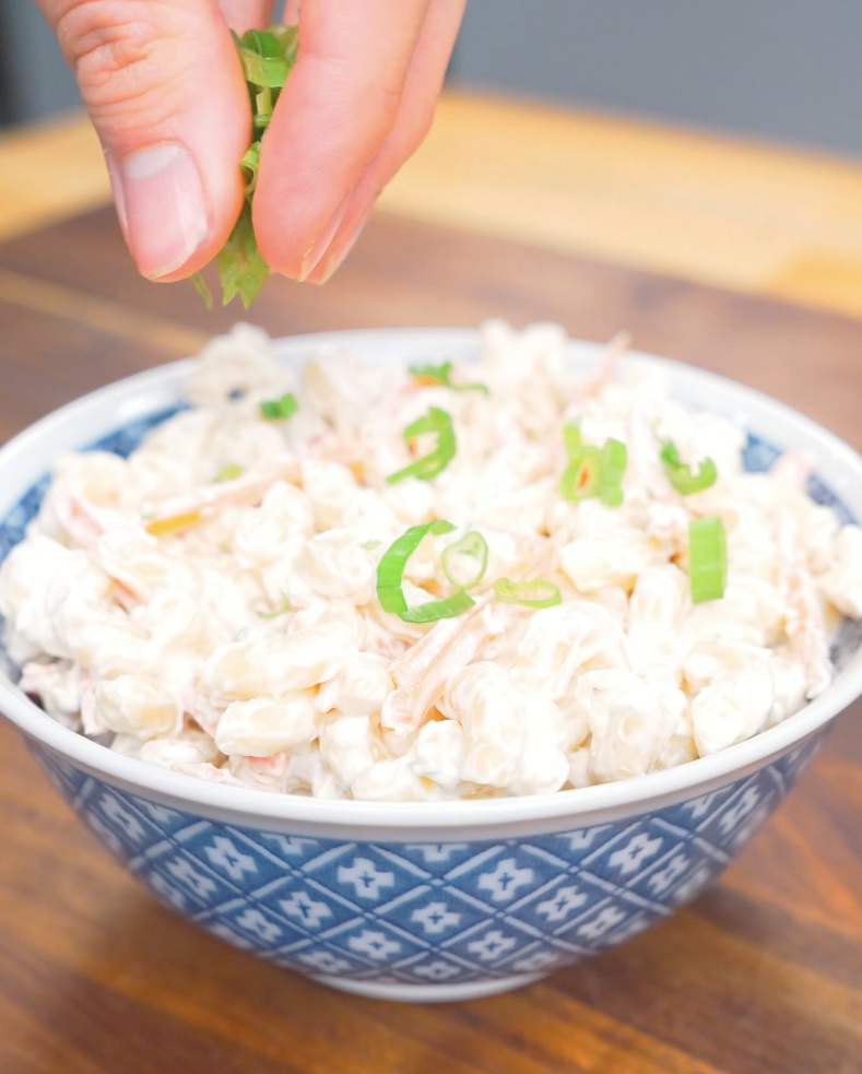 Sliced scallion greens being sprinkled over a chilled bowl of Hawaiian Mac Salad Recipe.