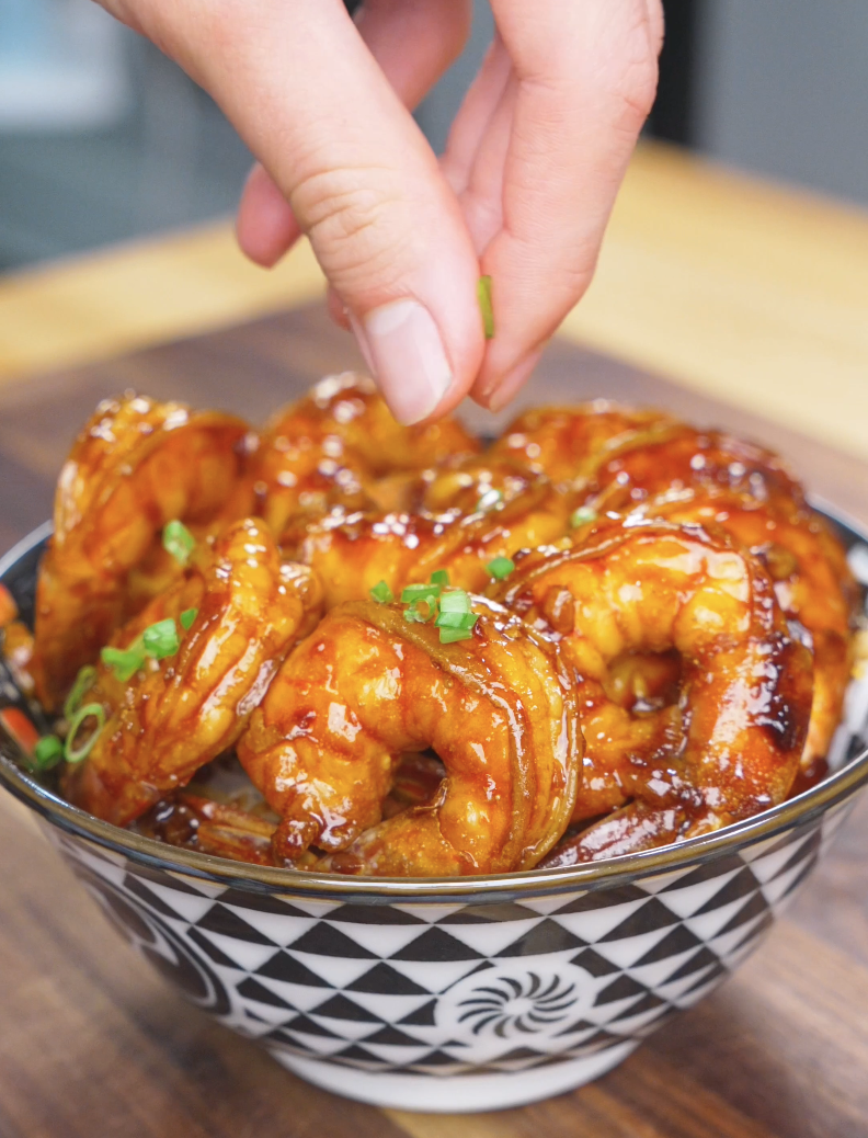 Sliced scallions being sprinkled over a rice bowl of Honey Garlic Shrimp Recipe.