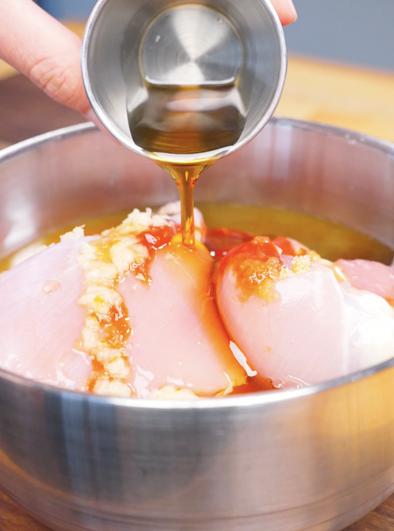 Marinade being poured over raw chicken with garlic and ginger in a bowl for Huli Huli Chicken Recipe.