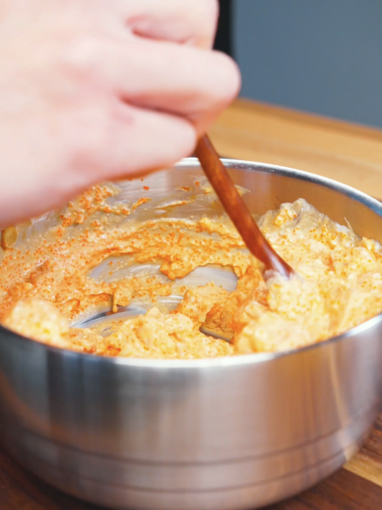 Spicy mayo, tobiko, and salmon being stirred together in a metal bowl for Creamy Salmon Poke Recipe.