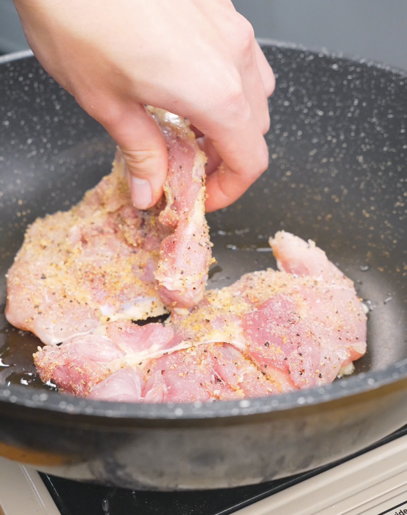 Seasoned chicken thighs being laid into a hot pan to sear for Creamy Garlic Chicken Pasta Recipe.
