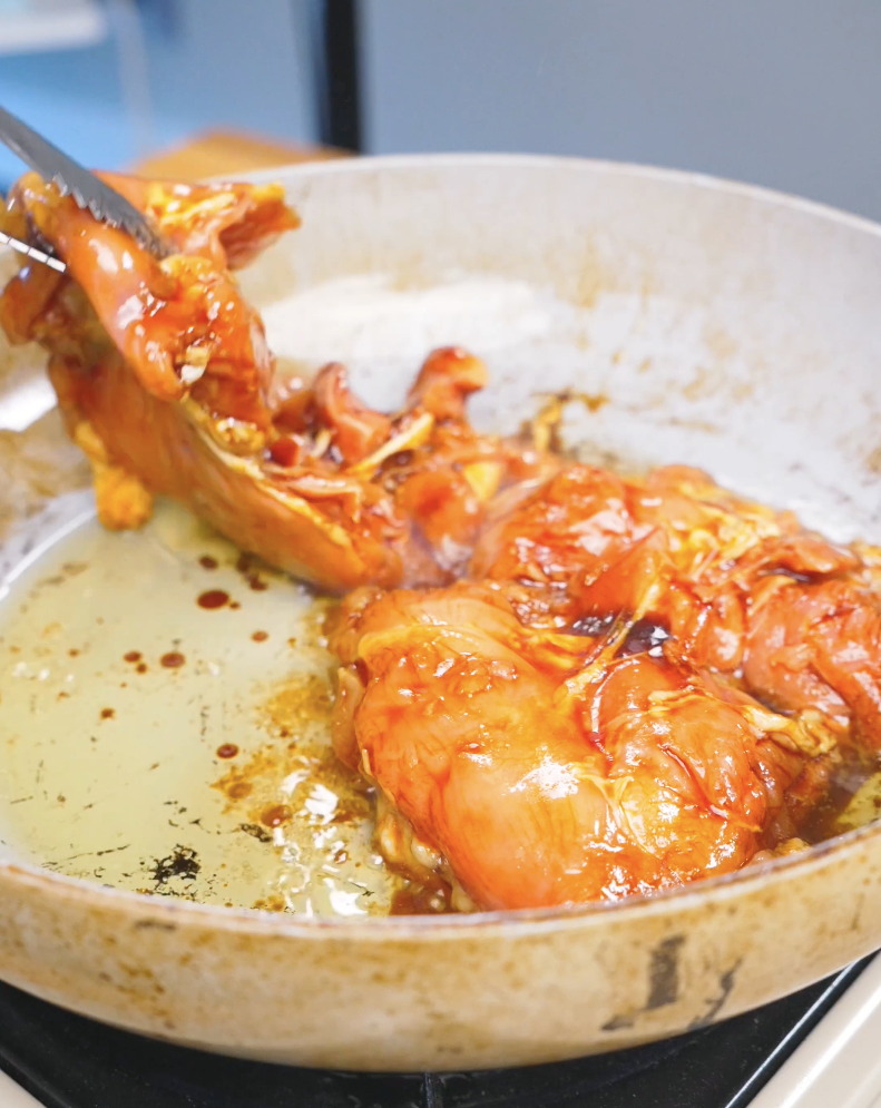 Marinated chicken being seared in a pan with tongs while making Huli Huli Chicken Recipe.
