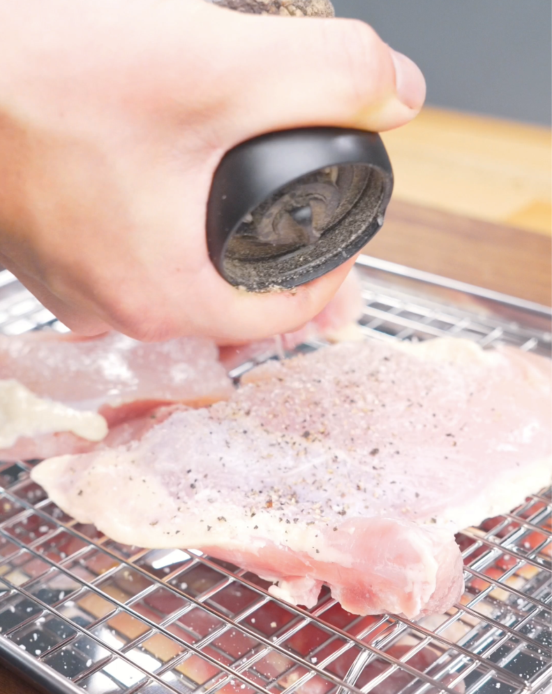 Raw chicken thighs being seasoned with salt and black pepper while preparing Creamy Garlic Chicken Pasta Recipe.