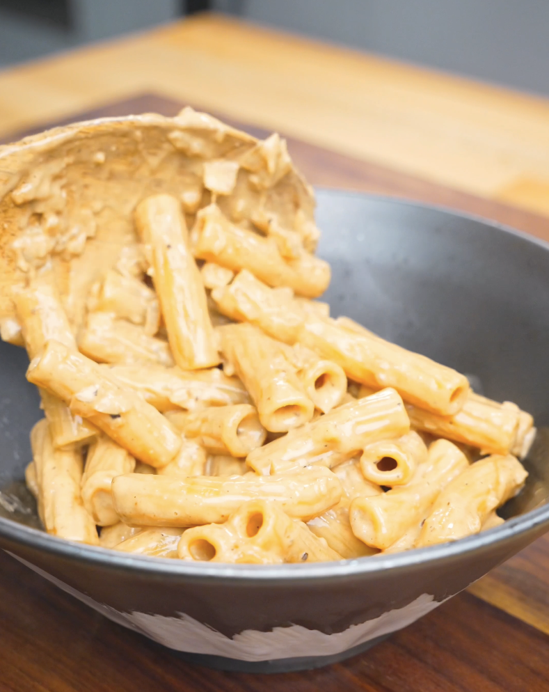 Creamy sauced rigatoni being spooned into a bowl for Creamy Garlic Chicken Pasta Recipe.