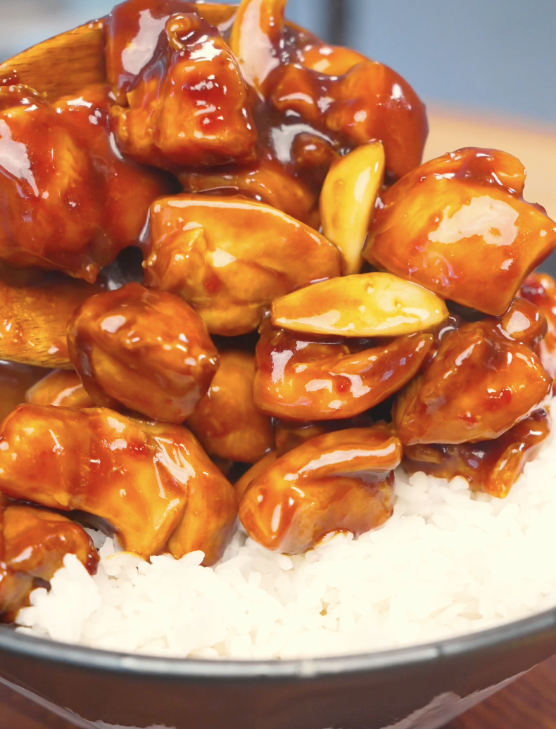 Glazed chicken and garlic cloves being spooned over steamed rice for Sticky Garlic Chicken Recipe.