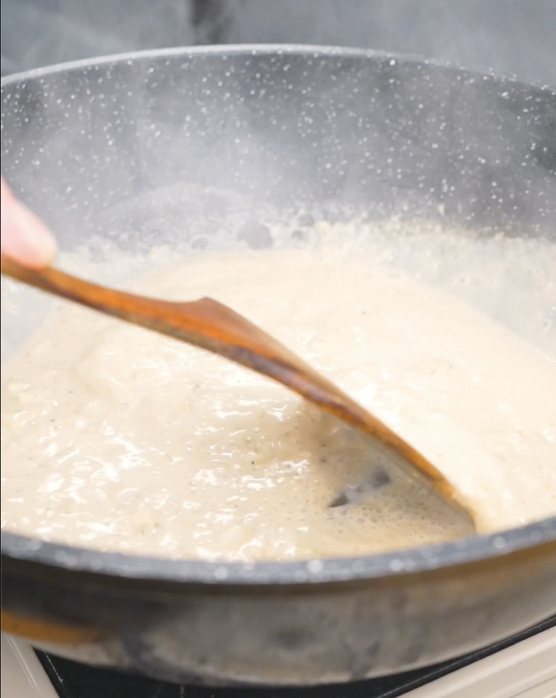 A garlic cream sauce simmering and thickening in the pan while making Creamy Garlic Chicken Pasta Recipe.