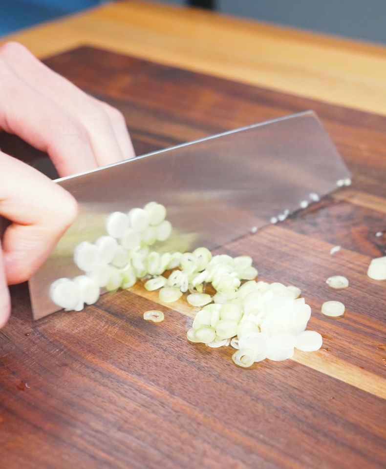 Green onions being thinly sliced on a cutting board for Creamy Salmon Poke Recipe.
