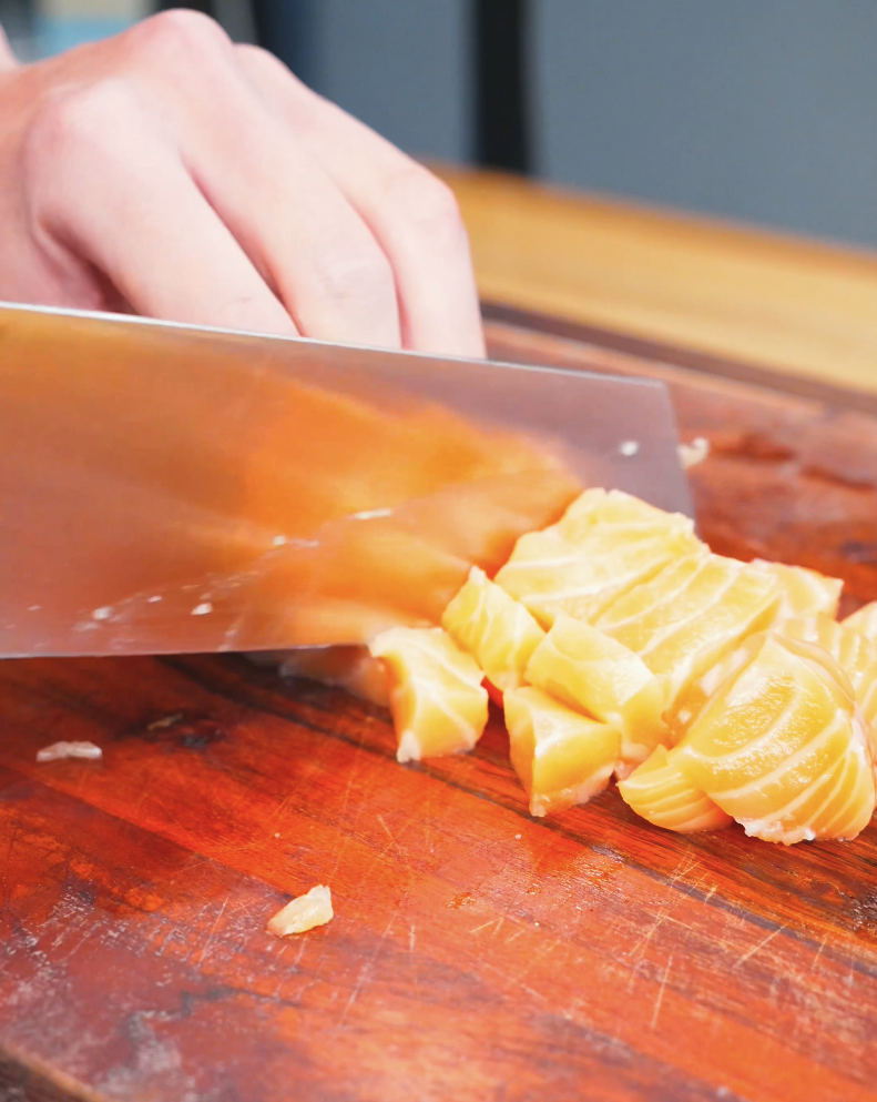 Fresh salmon being cubed with a knife on a wooden board while making Creamy Salmon Poke Recipe.