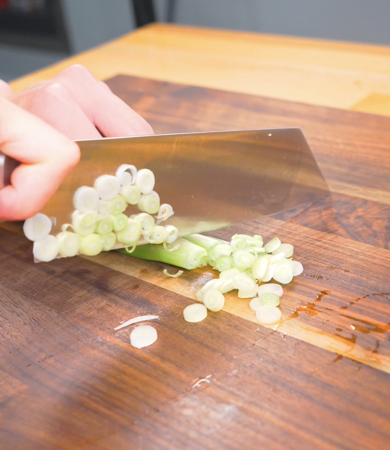 Scallions being thinly sliced on a cutting board for Hawaiian Mac Salad Recipe.