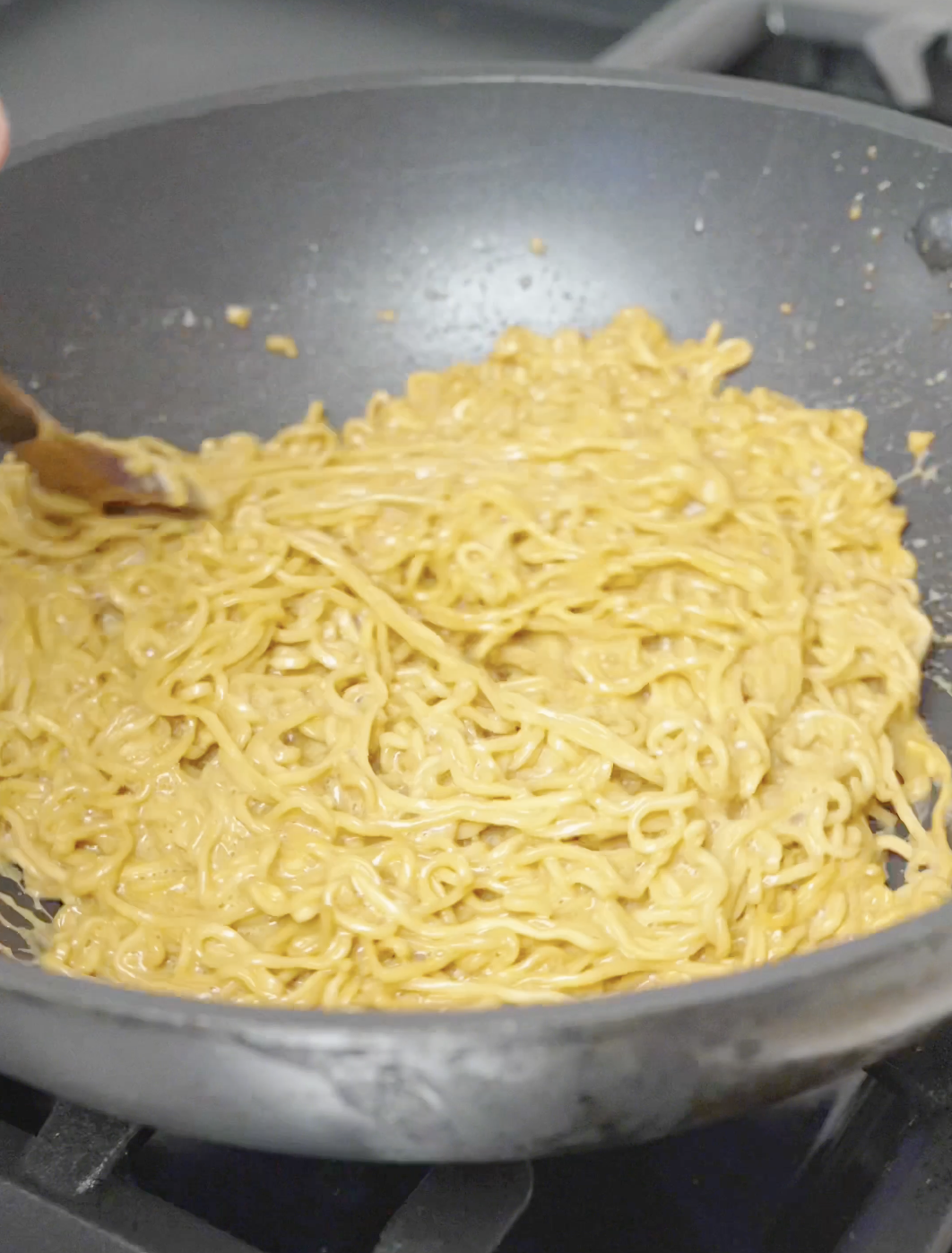 Instant noodles being tossed in a creamy garlic butter sauce until evenly coated.
