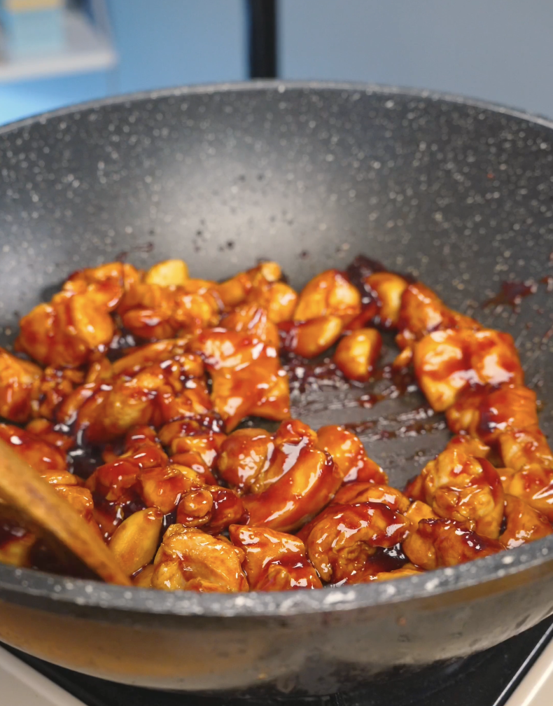 Chicken pieces being tossed in a thick, glossy sauce in the pan while making Sticky Garlic Chicken Recipe.
