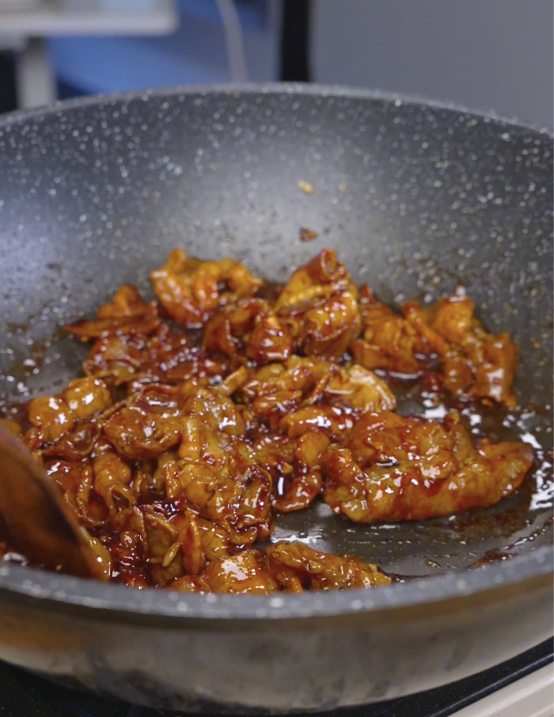 Pork belly strips being tossed in a glossy caramelized glaze in the pan while making Sticky Sweet Pork Belly Recipe.