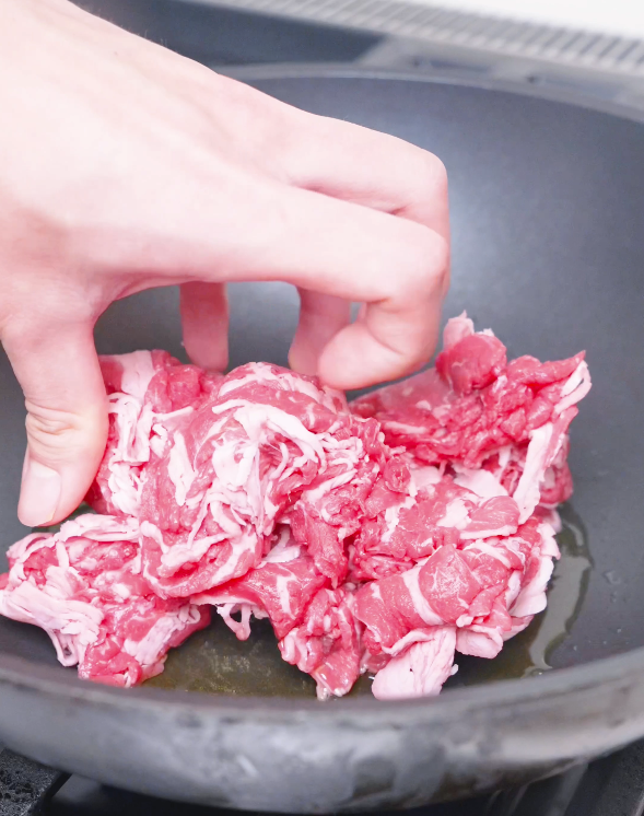 Thinly sliced raw beef being added to a hot oiled pan for Kimchi Beef Stir Fry Recipe.