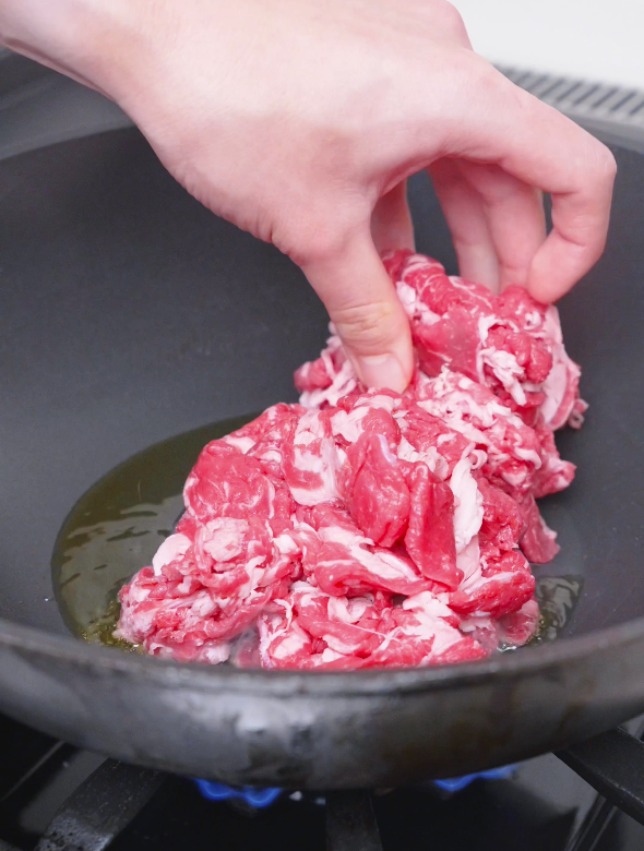Thinly sliced raw beef being laid into a hot oiled pan for Teriyaki Beef Recipe.