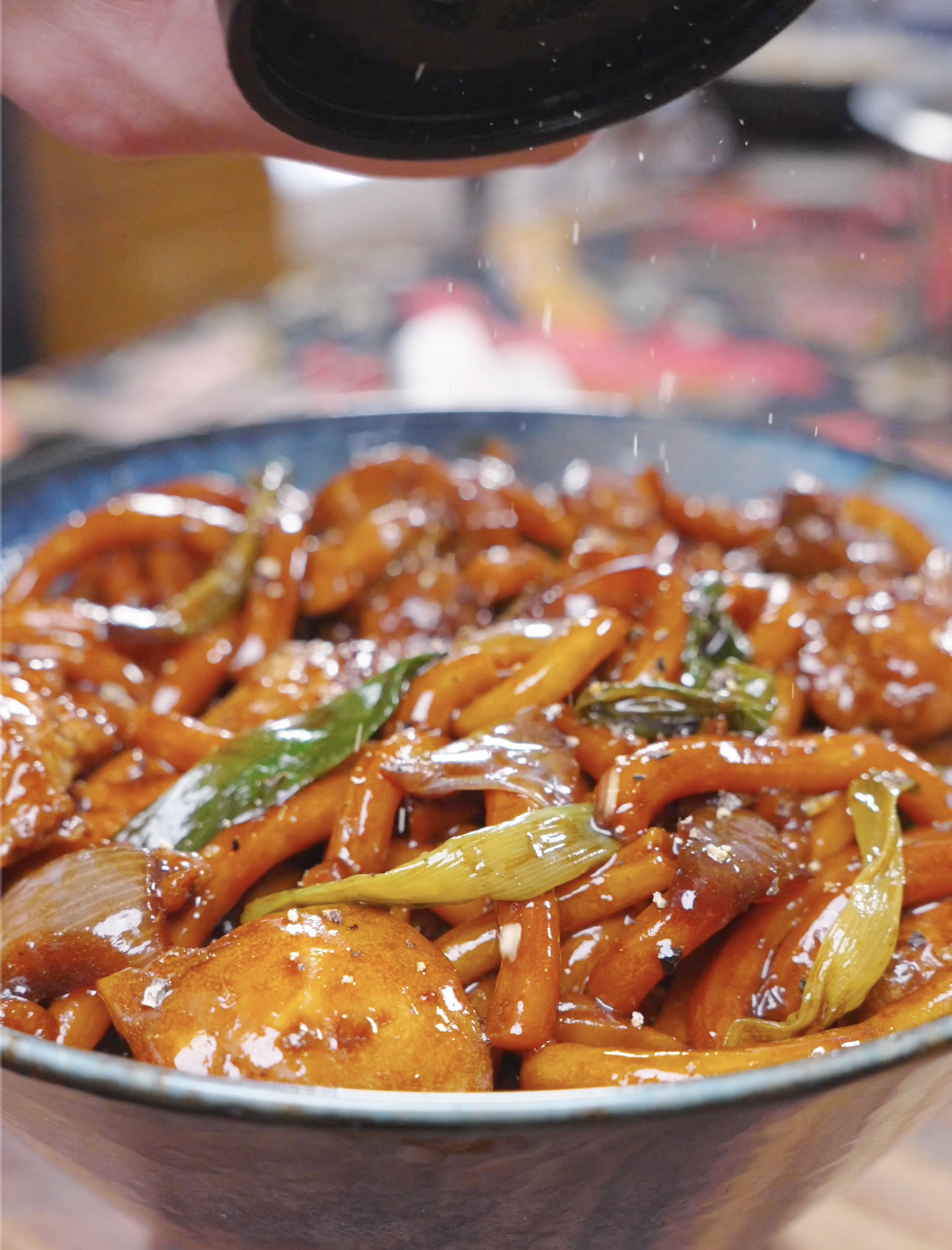 Freshly ground black pepper being sprinkled over the saucy udon for Black Pepper Chicken Udon Recipe.
