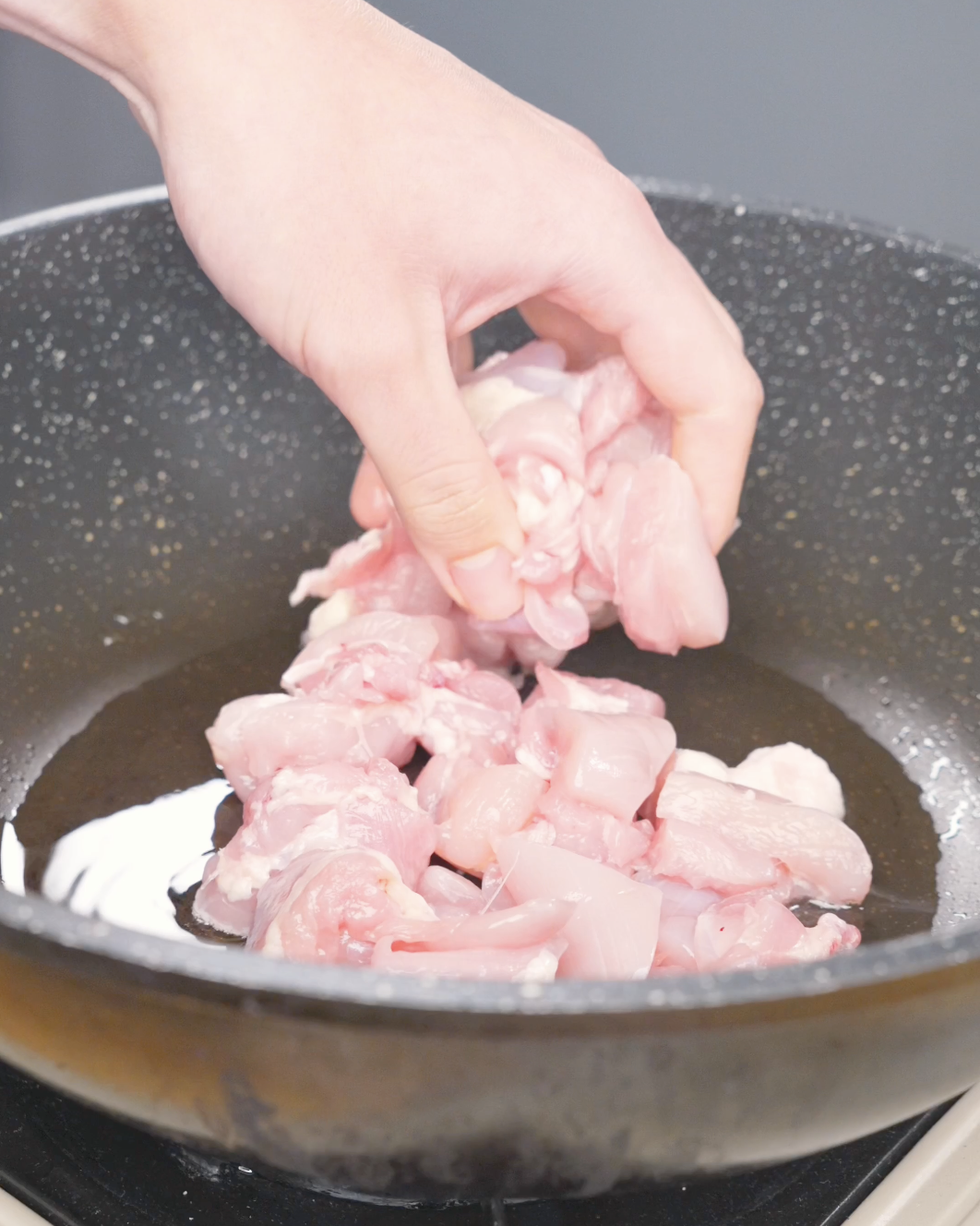 Bite-sized raw chicken pieces being added to an oiled pan for Honey BBQ Chicken Recipe.