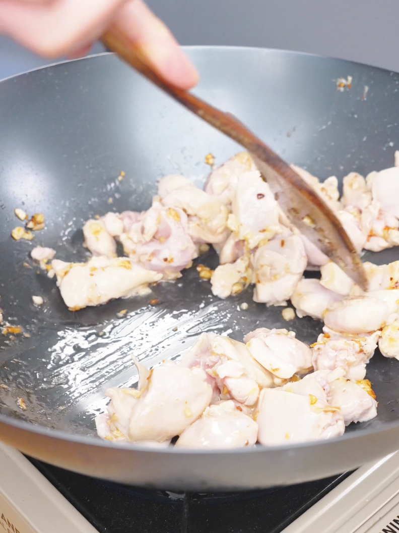 Bite-sized raw chicken pieces being added to the garlic in the pan for Sticky Orange Chicken Recipe.