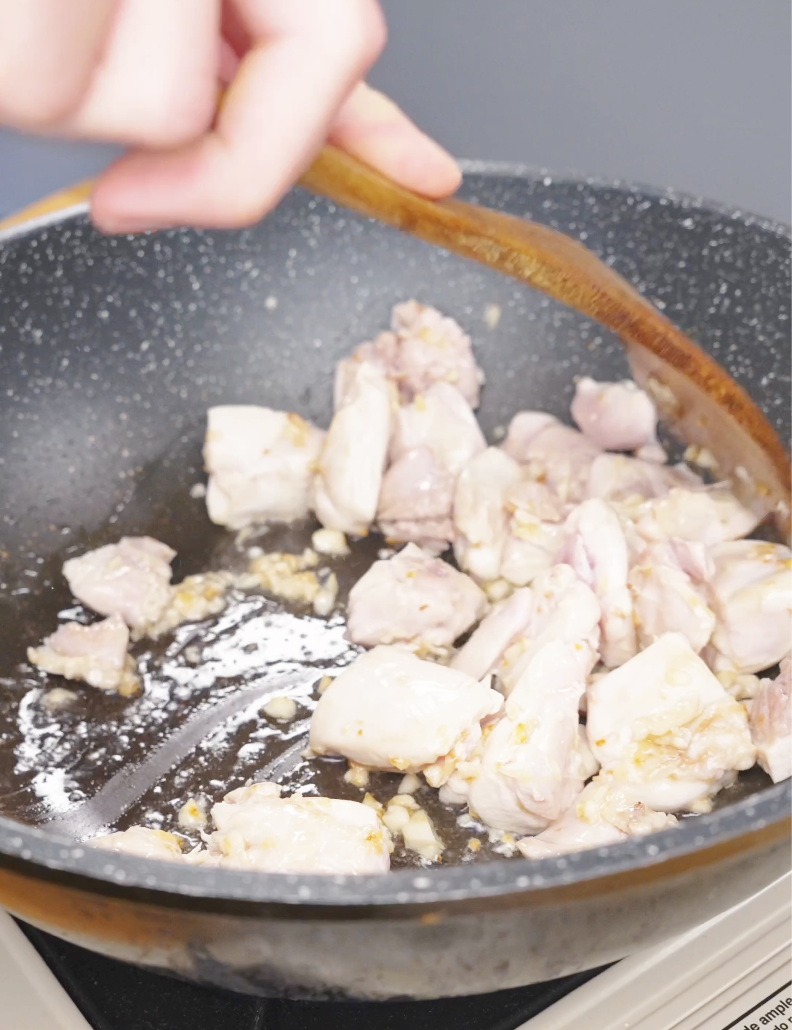 Bite-sized raw chicken pieces being added to the garlic in the pan for Sticky Soy Garlic Chicken Recipe.