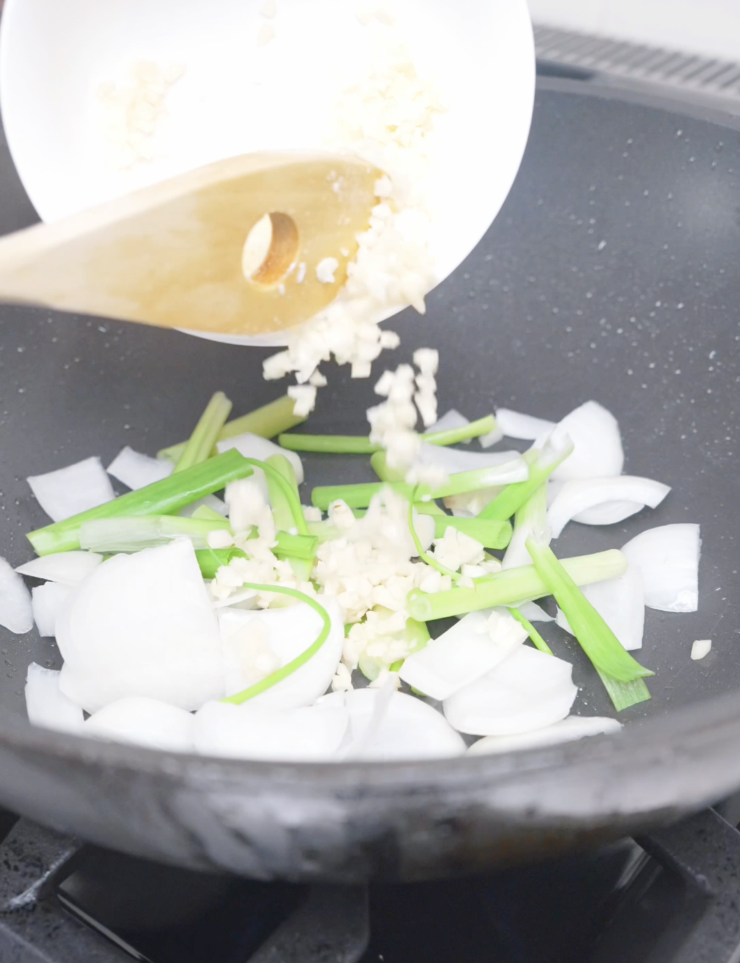 Minced garlic being added to onions and scallions in the pan for Black Pepper Chicken Udon Recipe.