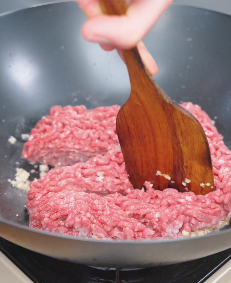 Raw ground beef being added to the garlic and butter in the pan for Garlic Butter Ground Beef Recipe.