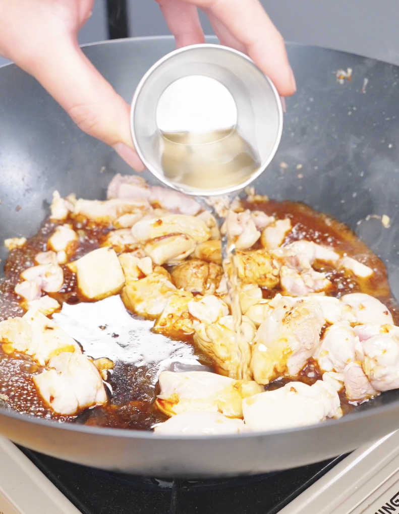 Orange juice being poured over the chicken and soy sauce in the pan for Sticky Orange Chicken Recipe.