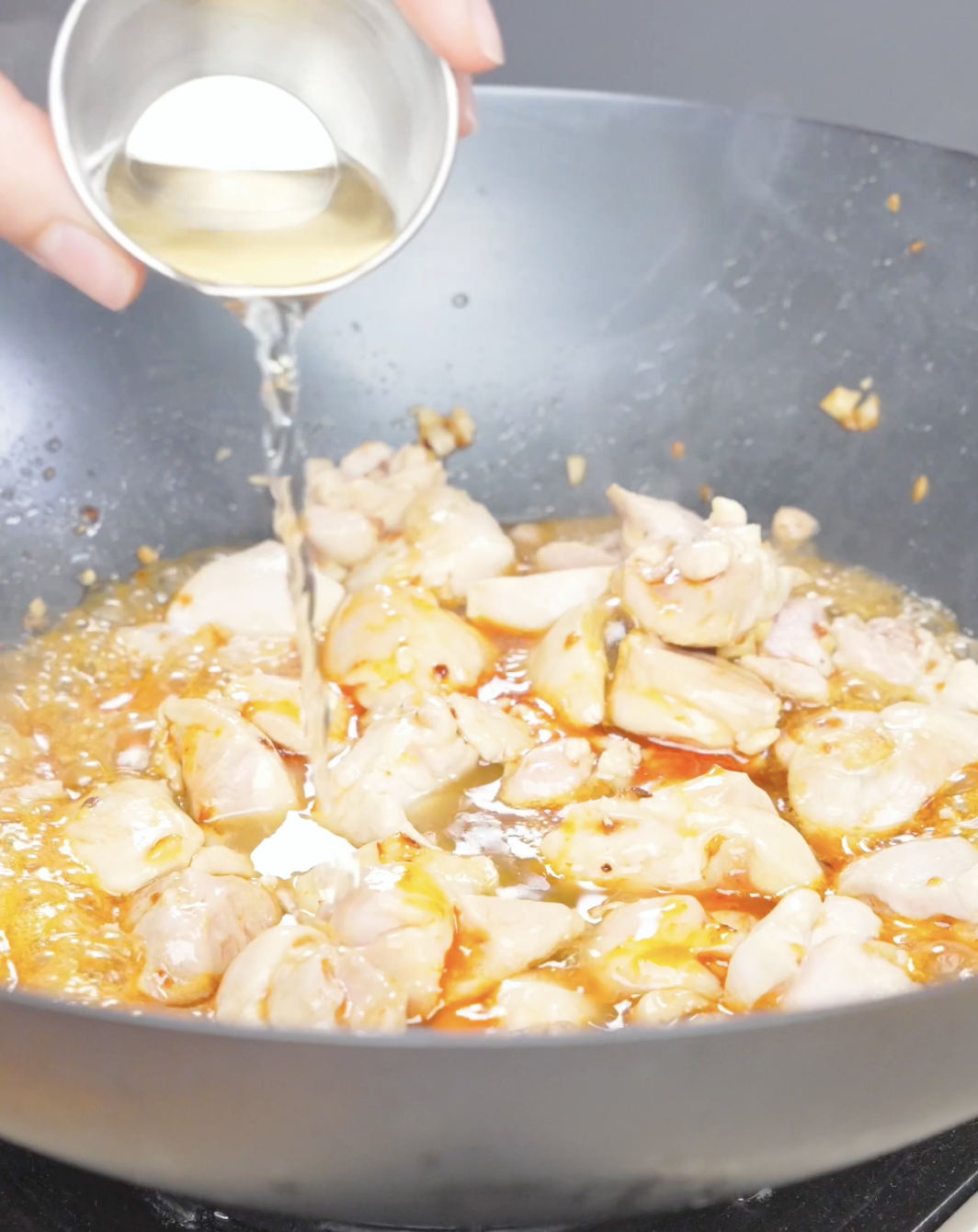 Rice vinegar being poured over the chicken and chili sauce in the wok while making Firecracker Chicken Recipe.