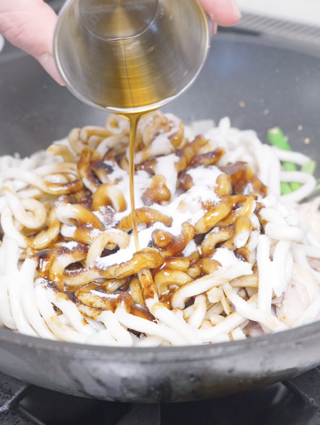 A golden sauce being poured over the udon noodles in the pan for Black Pepper Chicken Udon Recipe.