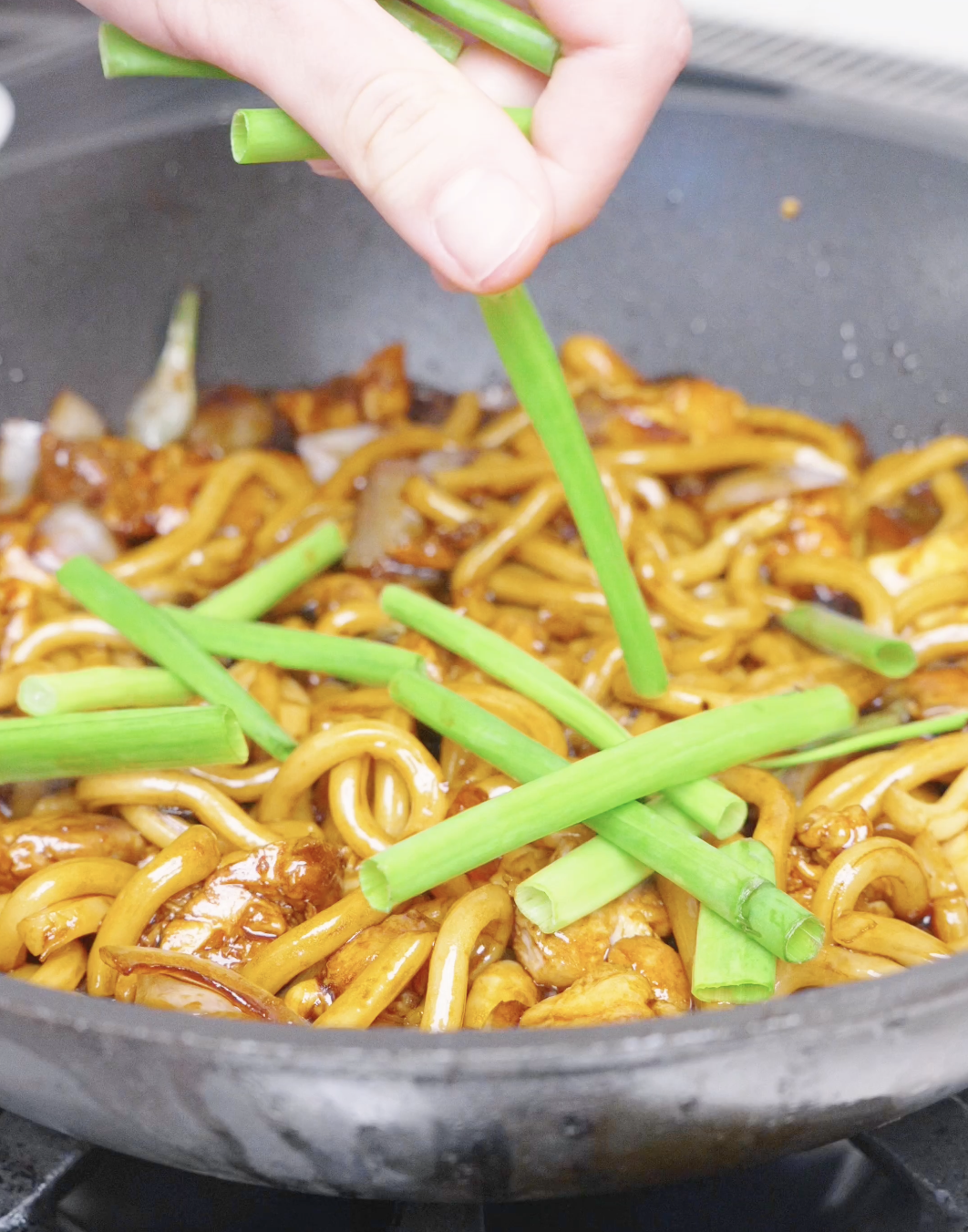 Cut scallion stalks being dropped into the saucy udon for Black Pepper Chicken Udon Recipe.