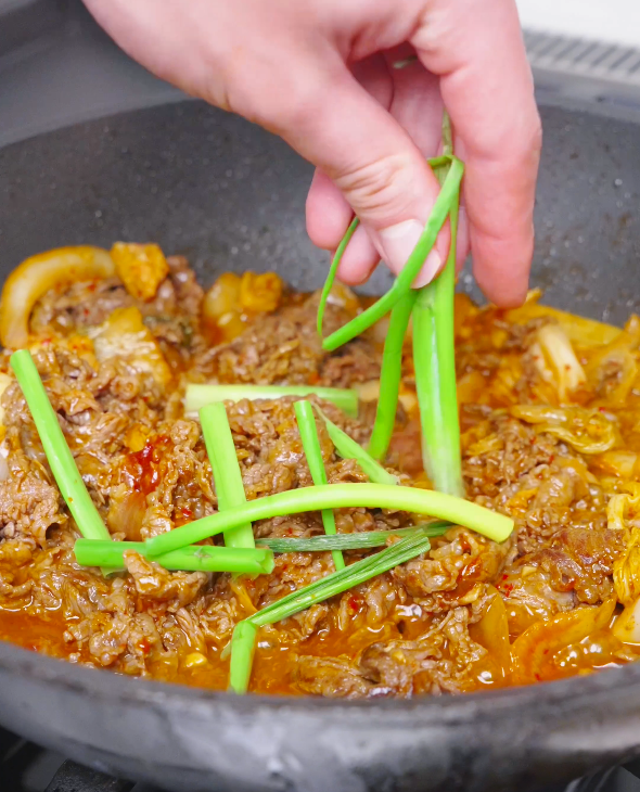 Cut scallions being dropped into the simmering red sauce for Kimchi Beef Stir Fry Recipe.