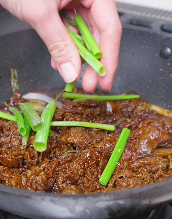 Cut scallion stalks being dropped into the glossy sauced beef for Teriyaki Beef Recipe.