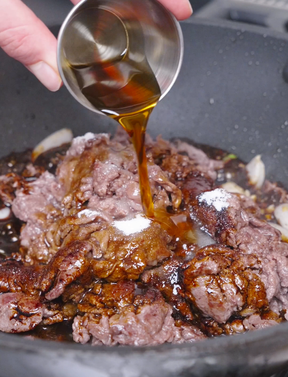 Dark teriyaki sauce being poured over the browned beef and sugar in the pan for Teriyaki Beef Recipe.