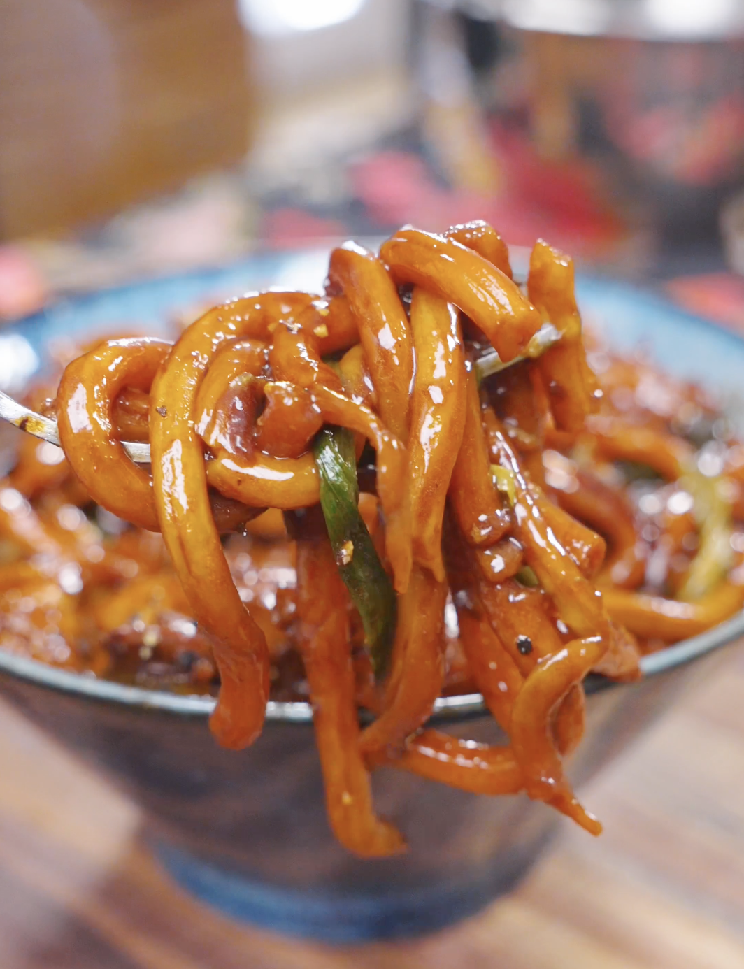 A fork lifting a twirl of glossy udon noodles above the bowl of Black Pepper Chicken Udon Recipe.