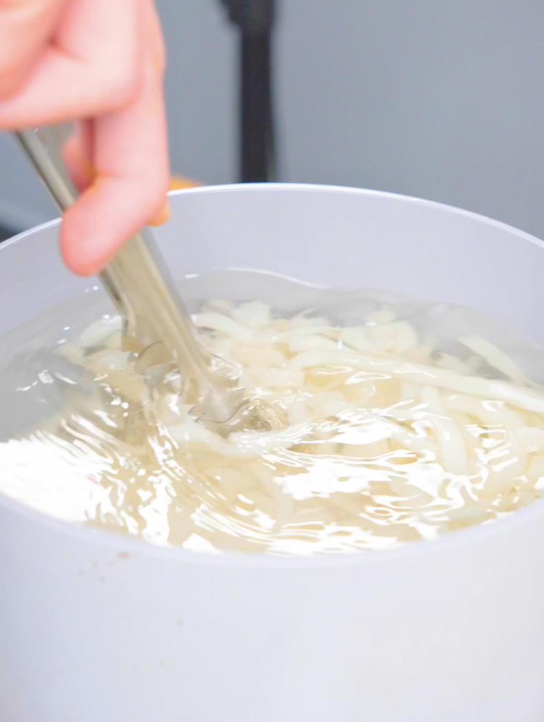 Udon noodles being cooked and loosened with tongs in boiling water for Creamy Miso Butter Noodles Recipe.