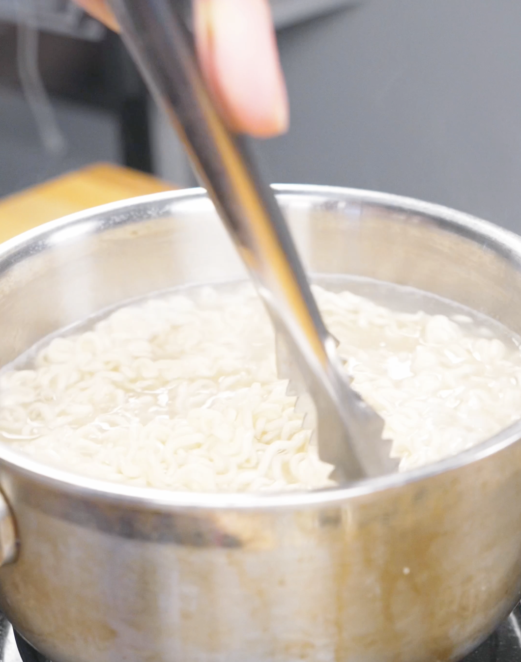 Ramen noodles being loosened with tongs in a pot of boiling water for Soy Butter Noodles Recipe.