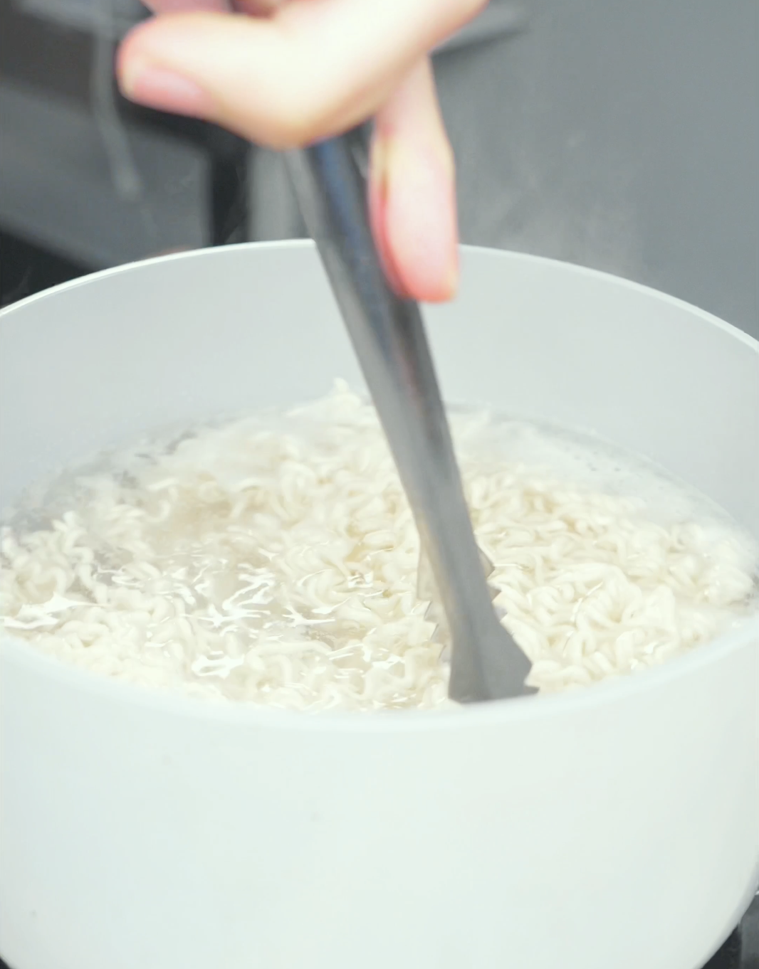 Ramen noodles being loosened with tongs in a pot of boiling water for Spicy Peanut Noodles Recipe.