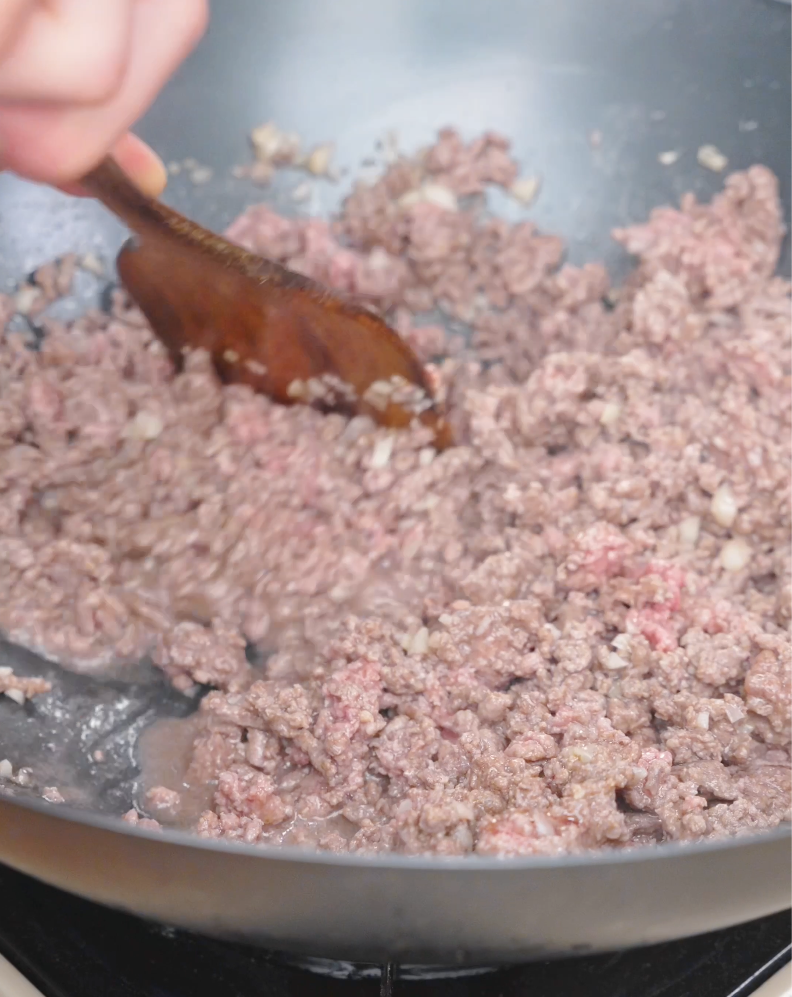 Ground beef being broken up and browned with a wooden spatula for Garlic Butter Ground Beef Recipe.