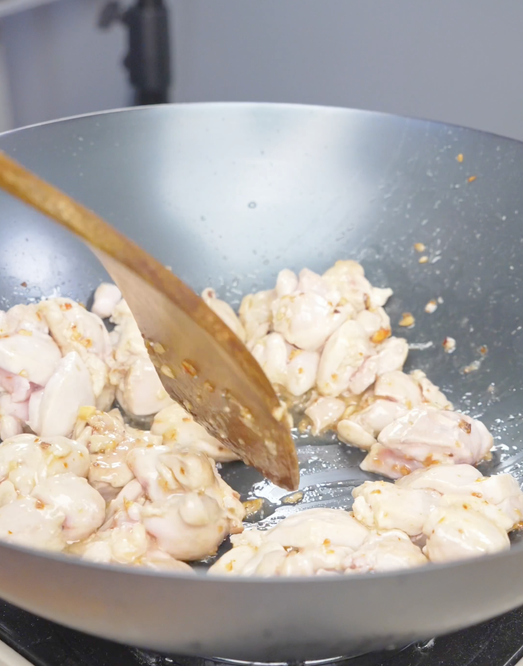 Chicken pieces being stirred with a wooden spatula as they cook for Firecracker Chicken Recipe.